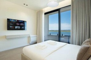 A hotel room with a bed, a flat-screen TV mounted on the wall, a window with a view of the sea, and a balcony with a table and chairs. - Luxury Villa with swimming pool, jacuzzi,breathtaking views. (Rrashbull)