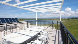 Ein überdachter Außenbereich mit Tisch und Stühlen, mit Blick auf ein Gewässer und die entfernte Landschaft.