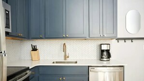 Een keuken met blauwe kastjes, een roestvrijstalen spoelbak, een koffiezetapparaat en een vaatwasser.