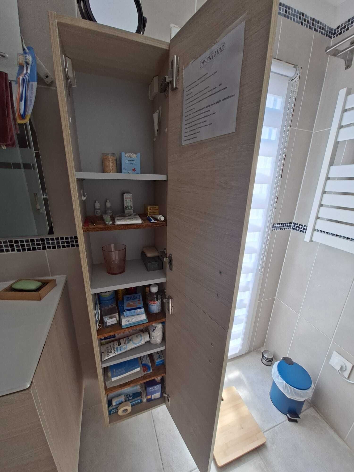 A bathroom with a wooden cabinet containing toiletries, a blue trash bin, and a white sink.