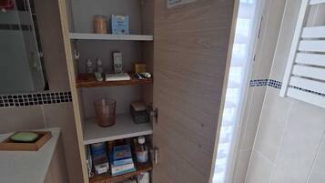 A bathroom with a wooden cabinet containing toiletries, a blue trash bin, and a white sink.