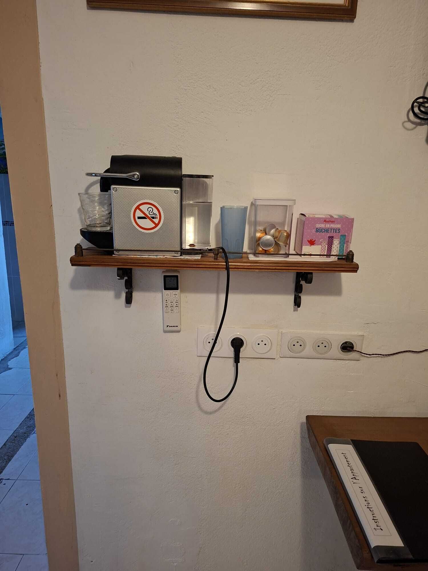 Seinälle kiinnitetty hylly, jossa on kahvinkeitin, lasipurkki ja pakkaus sokeripusseja.