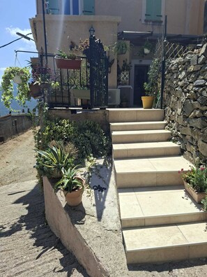 A stone staircase leading to a building with a balcony adorned with potted plants.
