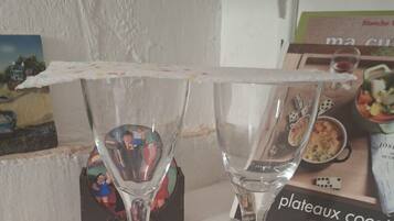 Two clear glass wine glasses on a table with a white tablecloth, a box of 'plateaux cocotte' in the background, and a small decorative item with a picture.