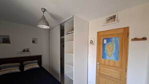 Un dormitori amb un llit, un armari, una porta de fusta amb un mapa i una làmpada al sostre.