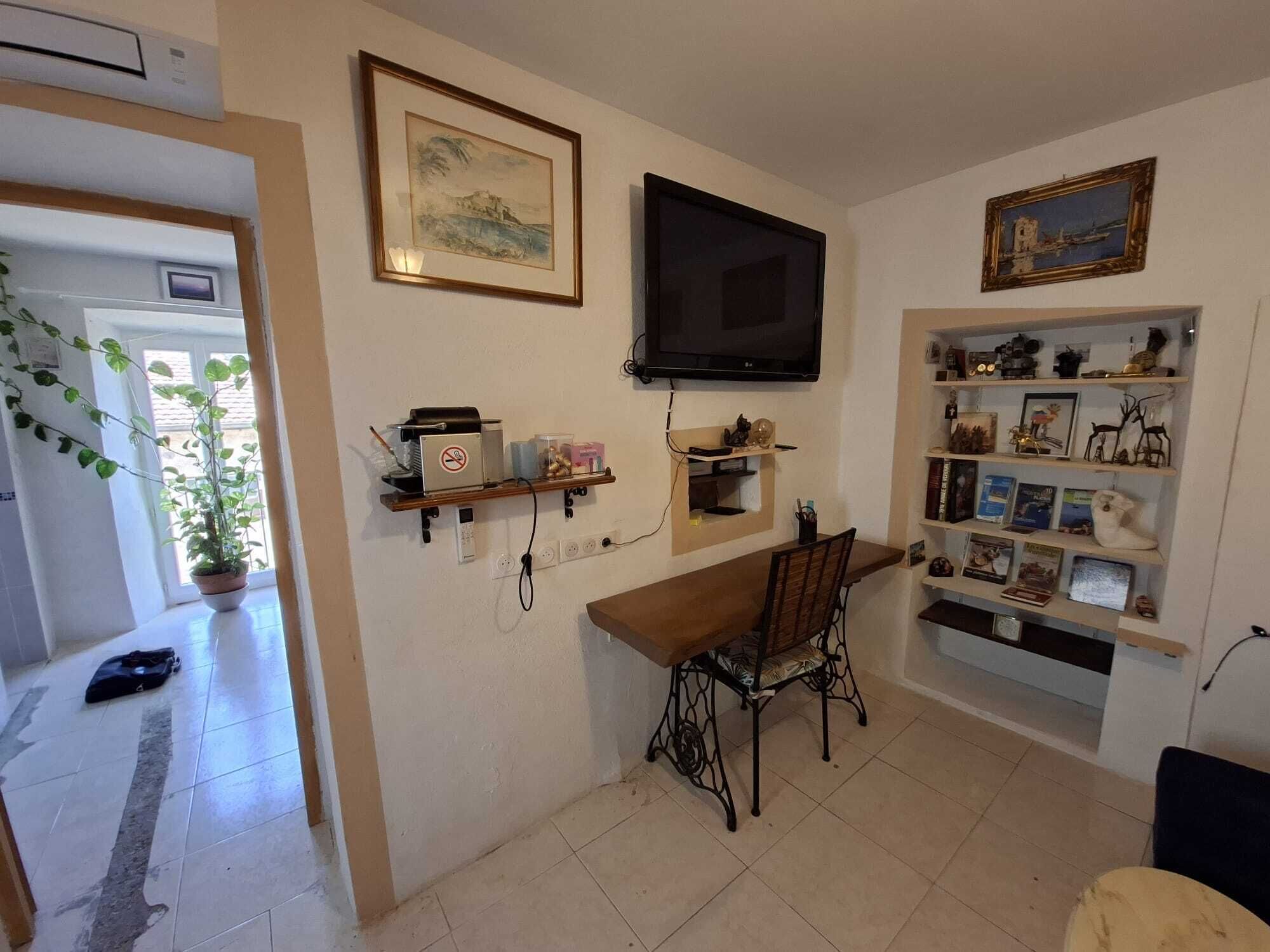 Ein Essbereich mit Tisch und Stühlen, einem an der Wand befestigten Fernseher und Regalen mit diversen Gegenständen.