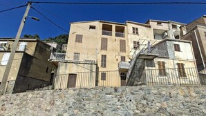 Un edifici d'alguns pisos amb balcons i una paret de pedra al davant.