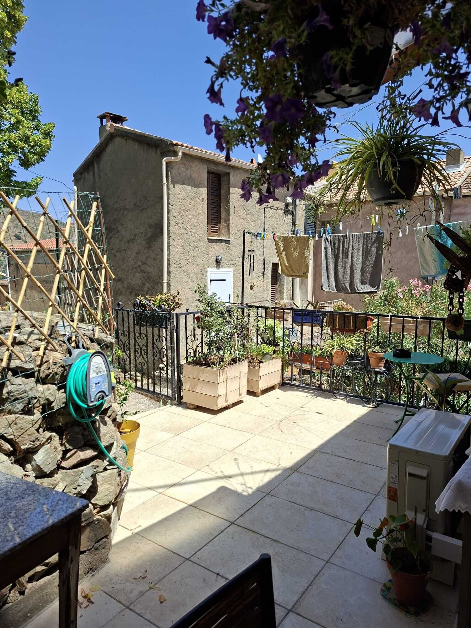 Une cour avec un mur en pierre, une clôture en métal et des plantes en pot.