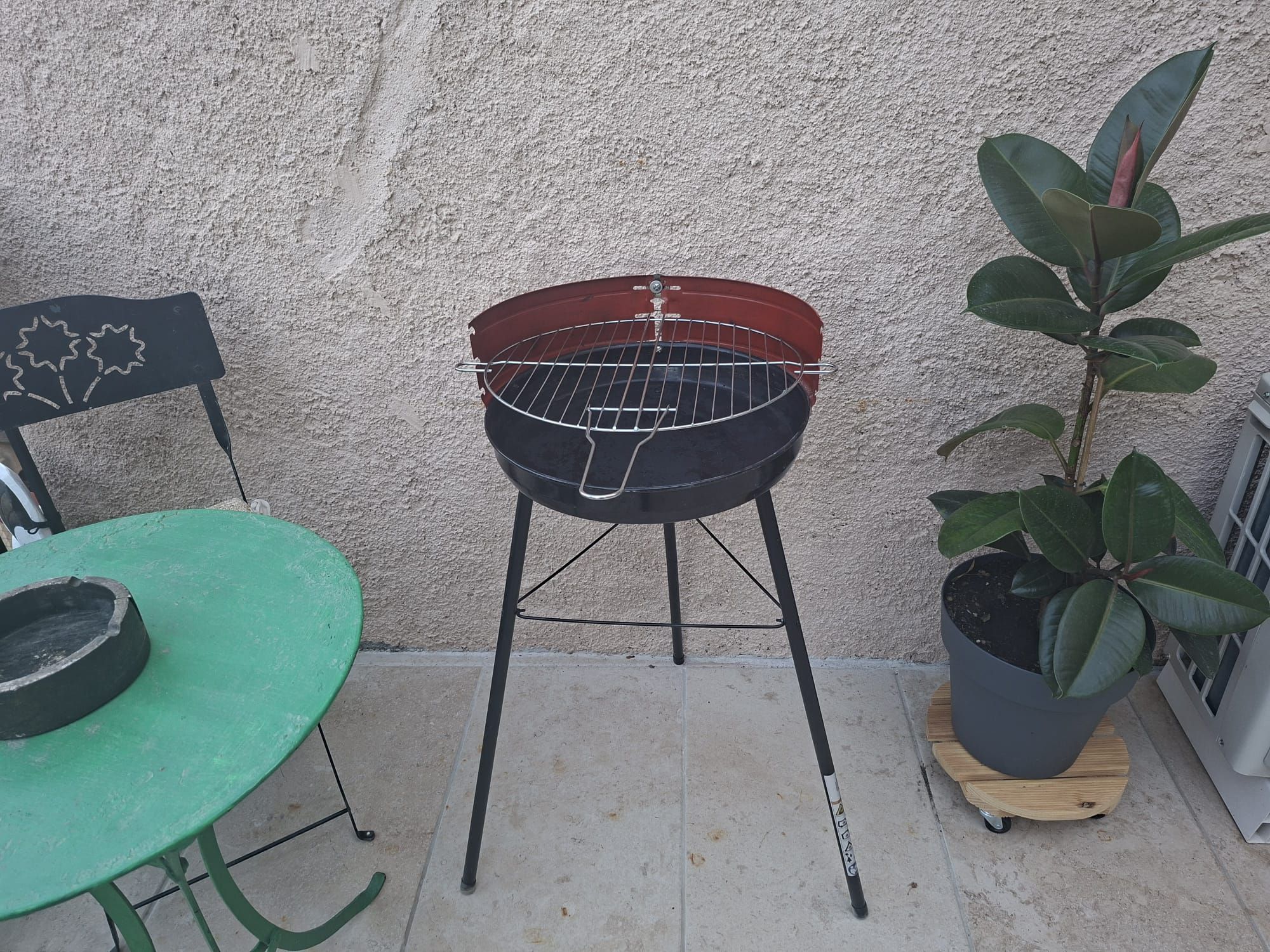 Una barbacoa sobre un suport, una taula verda i una planta en test.