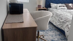 A bedroom with a bed, a desk, a chair, a nightstand, a lamp, and a painting on the wall. - Peaceful brand new home in a gated community in Azul (Pico Rivera)