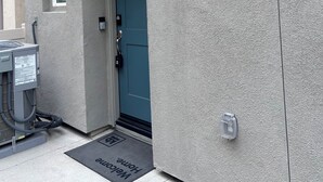 A building entrance with a blue door, a number sign '9339', a porch with wooden beams, and a black doormat with 'Welcome Home' text. - Peaceful brand new home in a gated community in Azul (Pico Rivera)