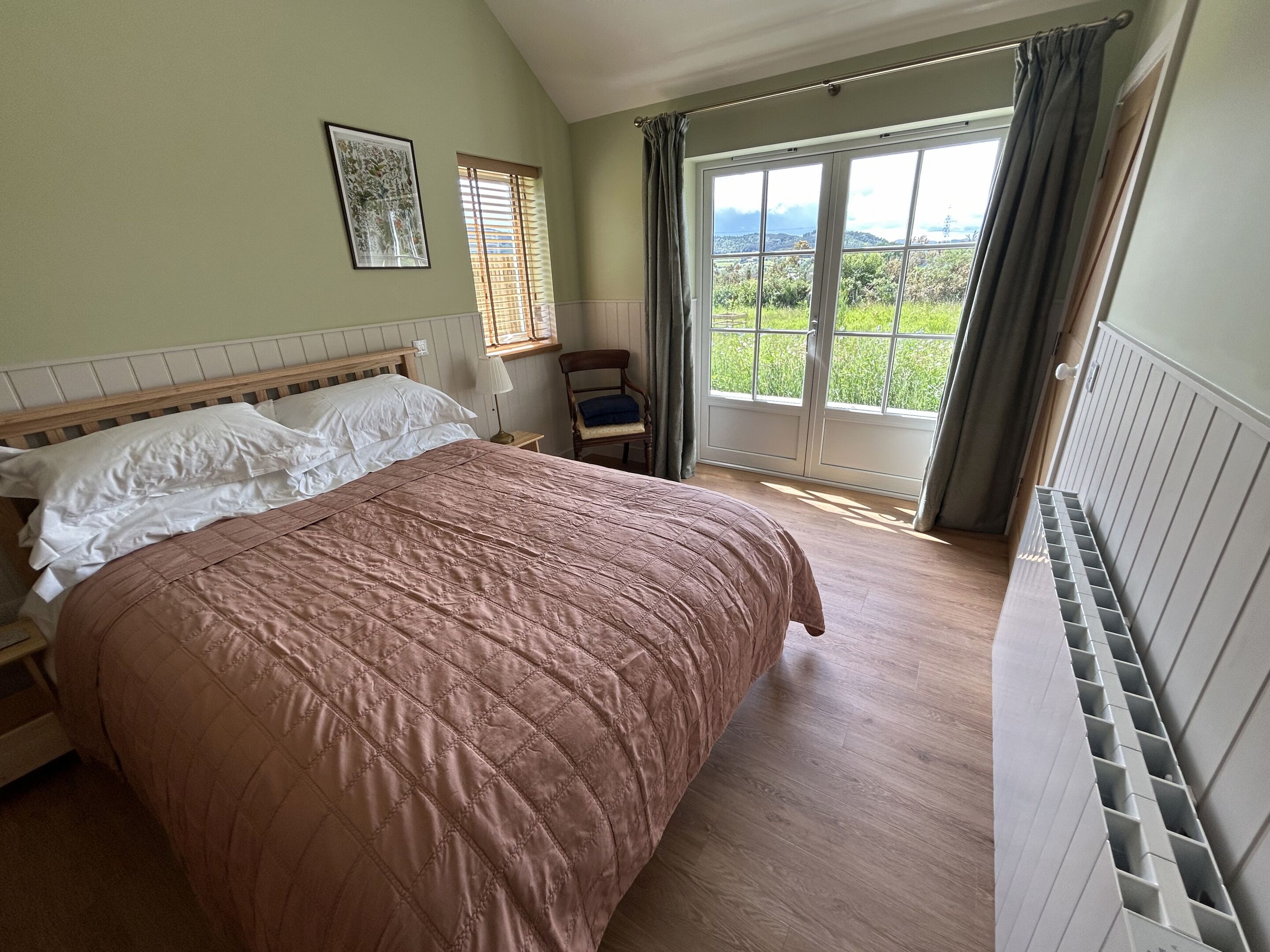 A bedroom with a large bed, a window with a view, a chair, and a radiator.