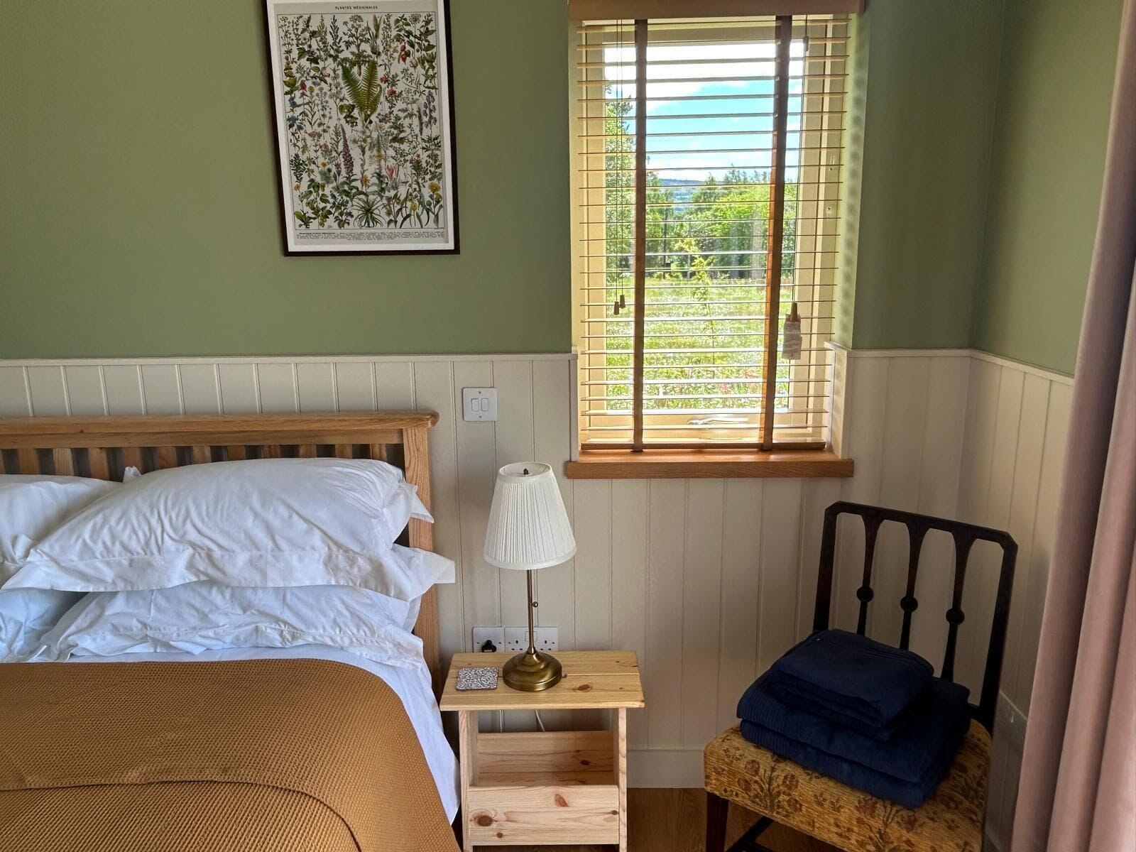 A bedroom with a bed, bedside table, lamp, and a window with blinds.