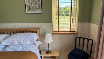 A bedroom with a bed, bedside table, lamp, and a window with blinds.