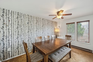 Ein Esszimmer mit Holztisch, Stühlen, Deckenventilator und einem Fenster mit Jalousien.