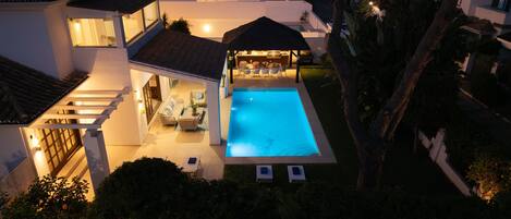 A residential property with a swimming pool, outdoor seating, and a covered patio area.