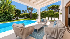 A poolside area with wicker furniture, a cactus, and a view of the pool and greenery. - Villa Marblanc by Vacation Marbella (Estepona)