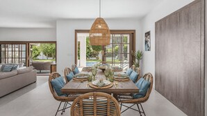 A dining area with a wooden table, wicker chairs, and a hanging light fixture. - Villa Marblanc by Vacation Marbella (Estepona)