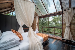 Un dormitorio con cama con dosel, suelo de madera y ventanas amplias que ofrecen vistas al exterior.