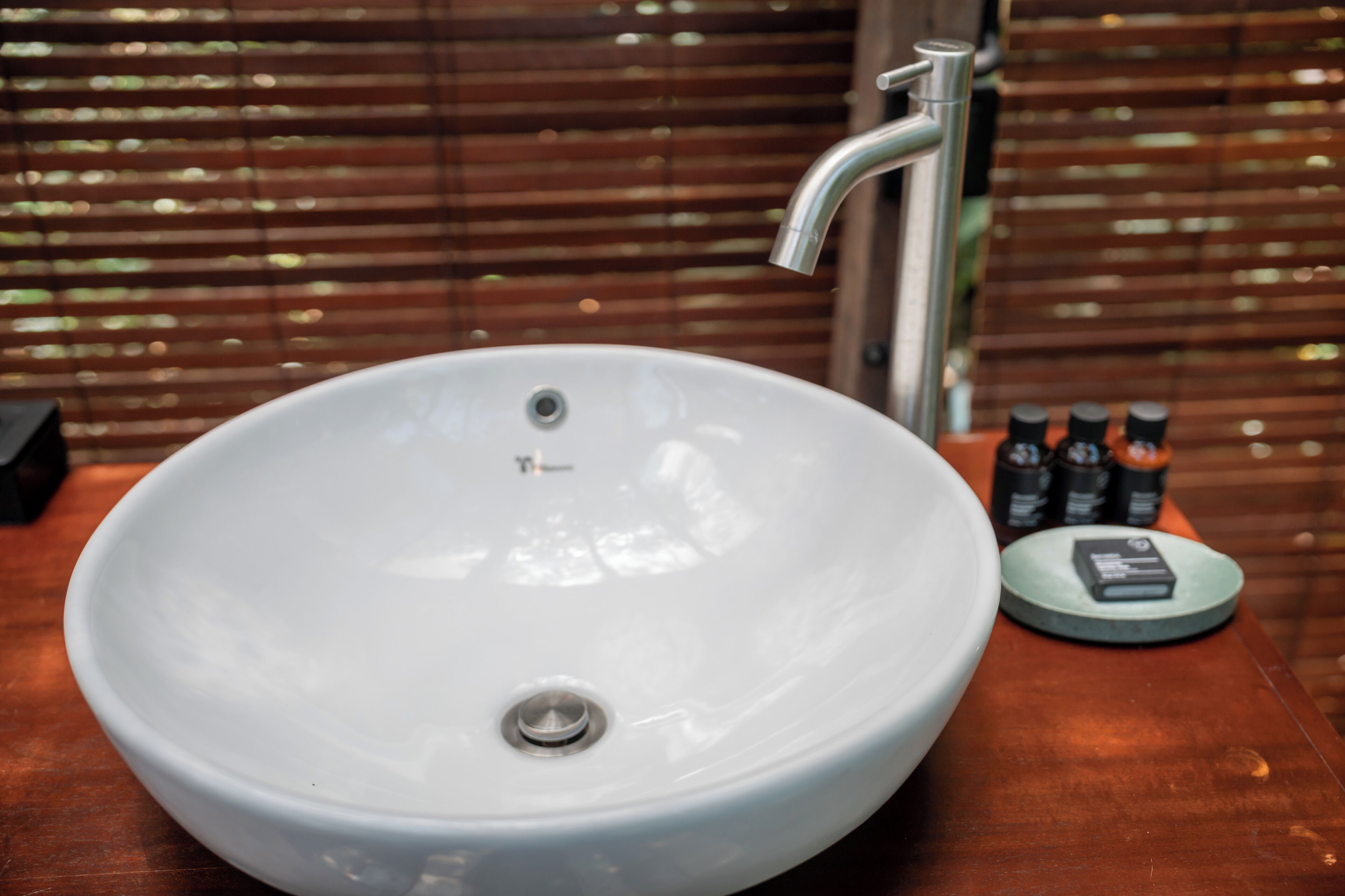 A white sink with a modern faucet, a soap dispenser, and a small round tray with a bottle.