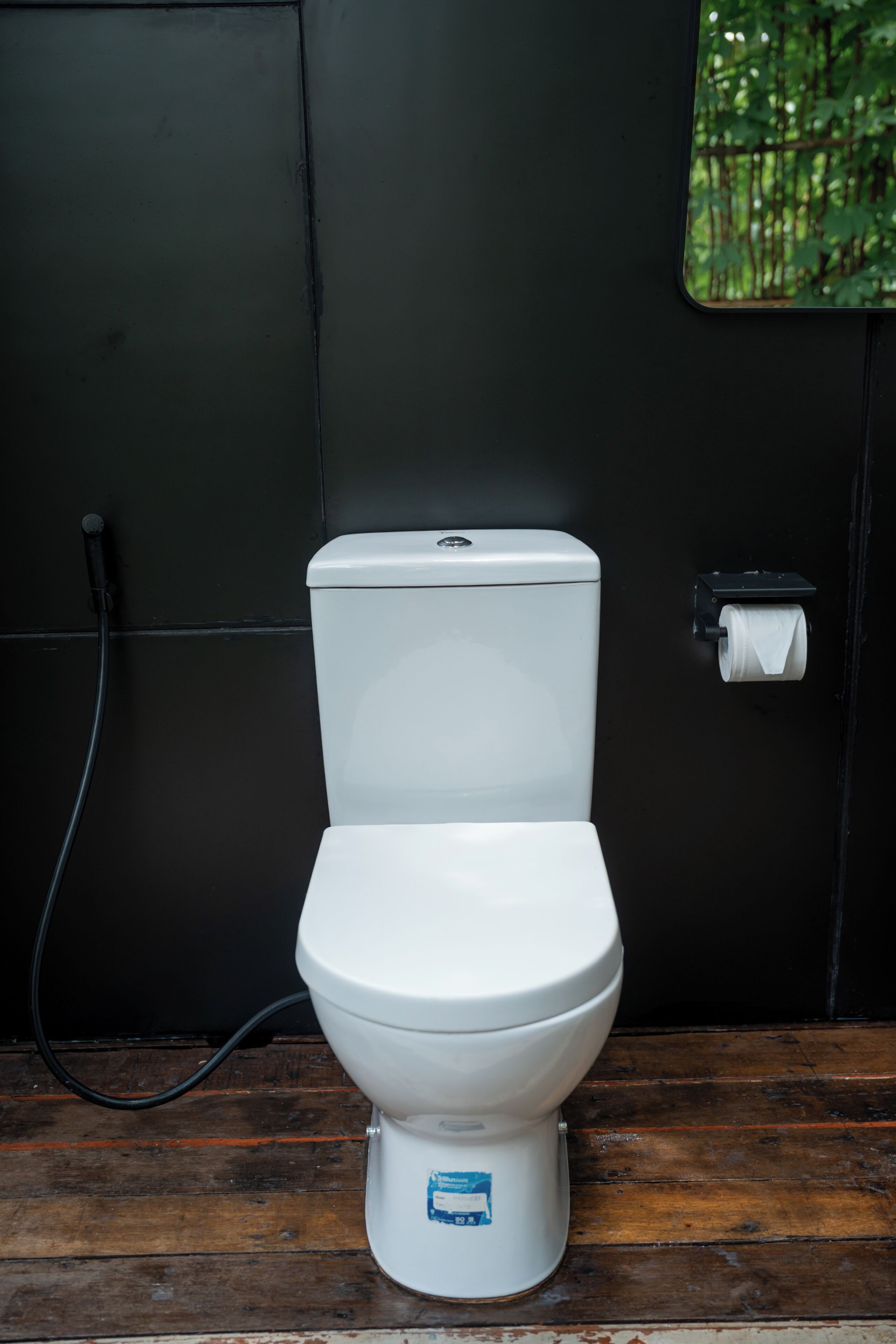 Sanitário branco num banheiro com parede preta e chão de madeira.