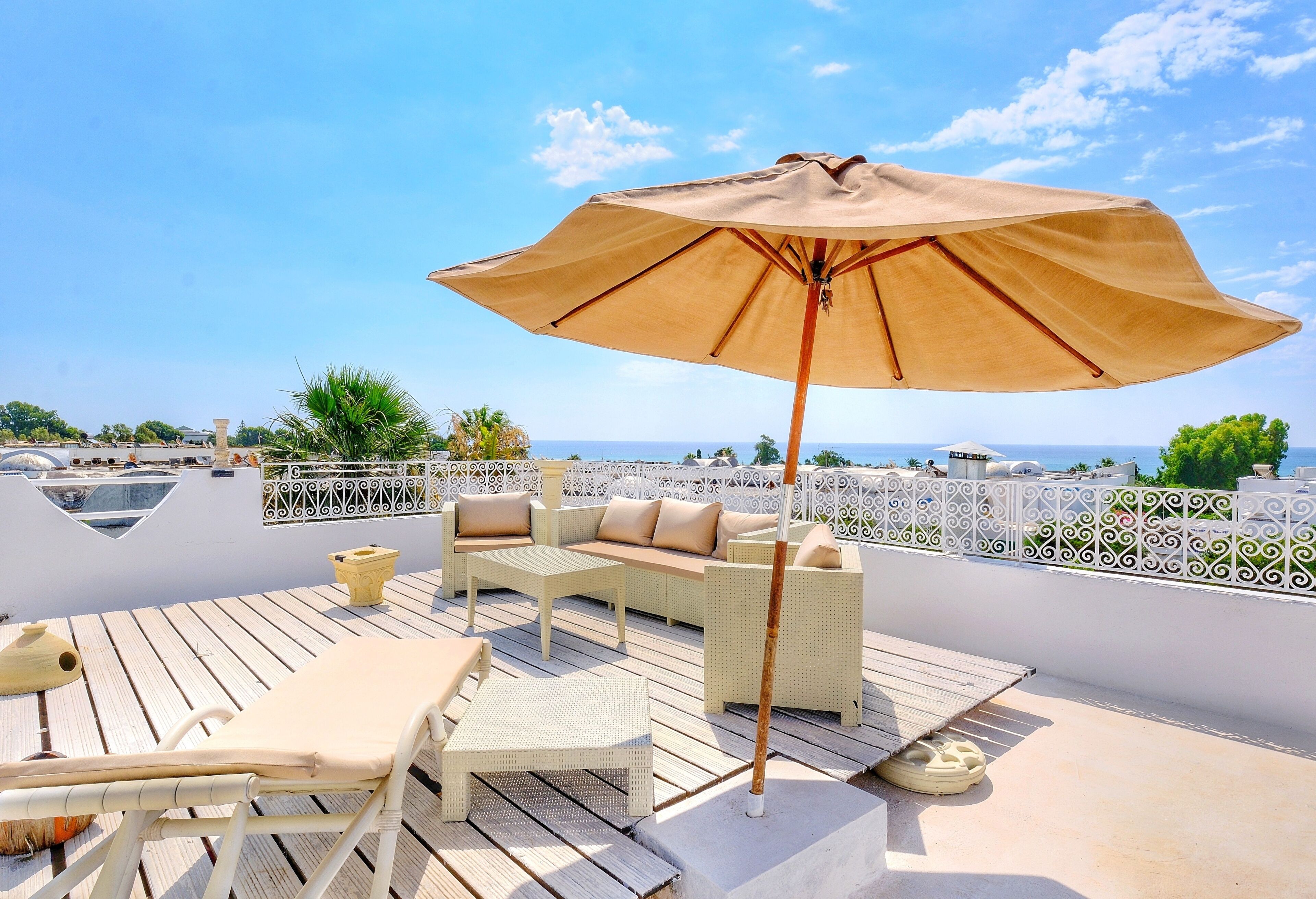 A rooftop terrace with outdoor furniture, a large umbrella, and a view of the sea.
