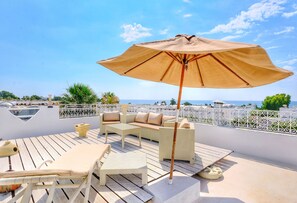 Une terrasse sur le toit, aménagée avec du mobilier d’extérieur, un grand parasol et offrant une vue sur la mer.