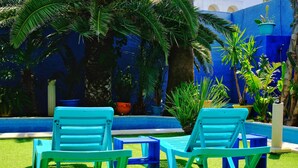 Zona junto a la piscina con dos sillones azules, una mesita y una pared azul.
