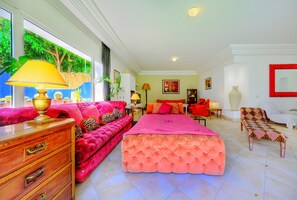 Un salon spacieux avec un grand lit, un canapé et un fauteuil. Une fenêtre offre une vue sur la verdure environnante.