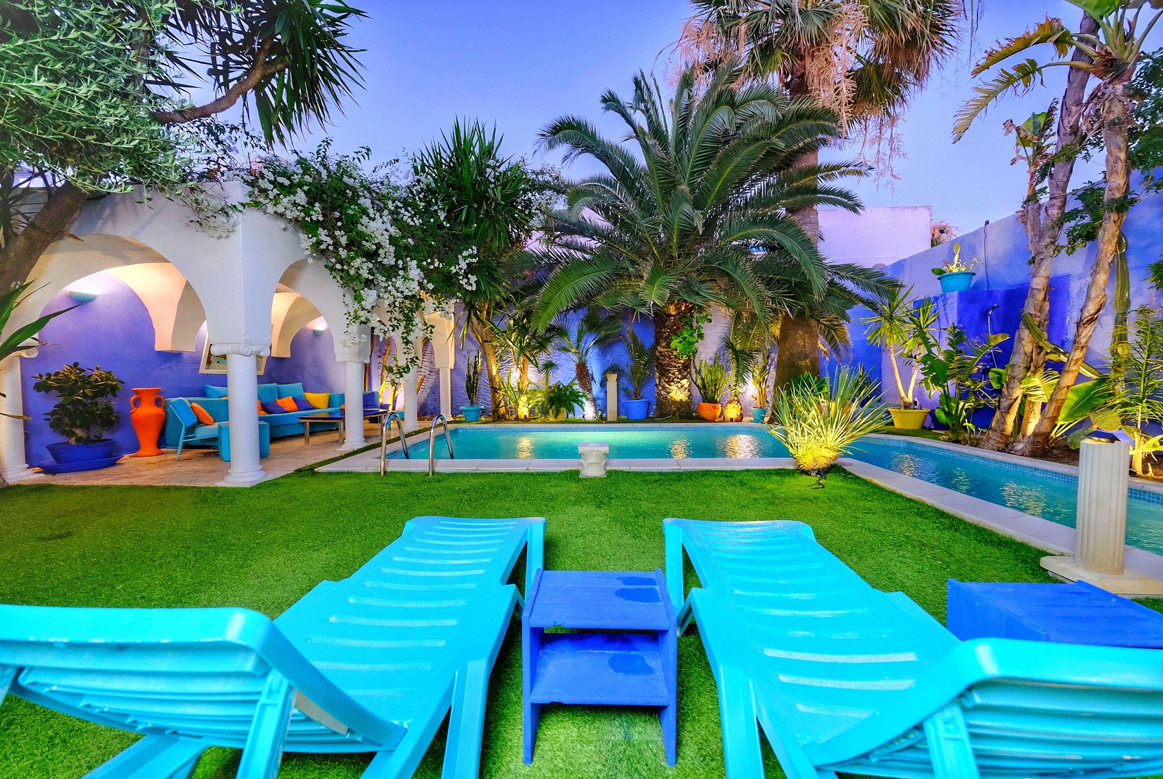 A pool area with lounge chairs, a pool, and tropical plants.