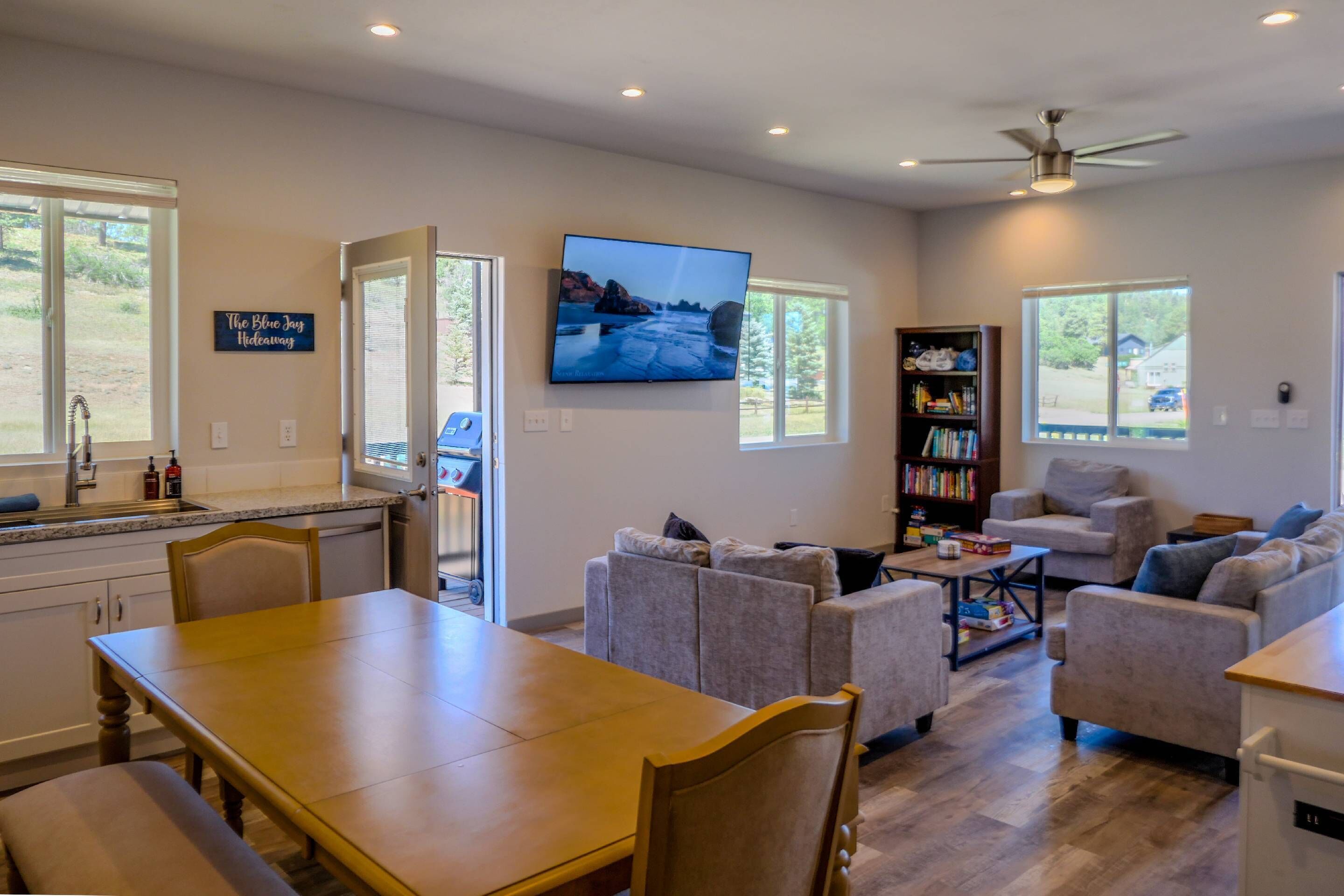 A modern living room with a flat-screen TV, a dining area, and a bookshelf.