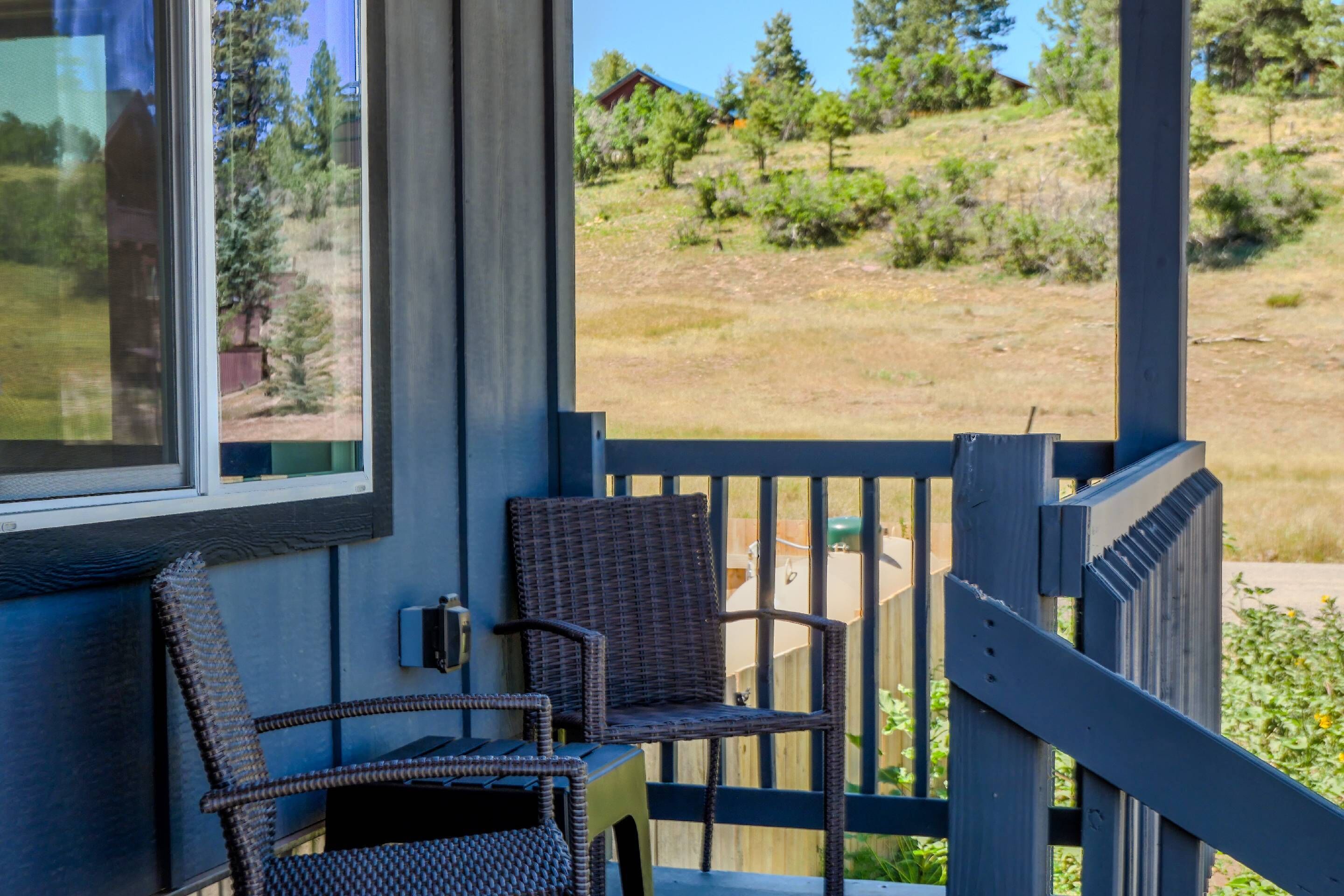 A balcony with wicker furniture, a view of a grassy area with trees, and a clear sky.