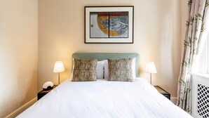 Ein Hotelzimmer mit einem Bett, zwei Nachttischlampen, einem gerahmten Kunstwerk über dem Bett und einem Fenster mit Vorhängen.