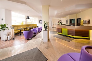 Eine Hotelhalle mit Empfangstresen, einer sitzgelegenen Zone in Lila und einem modernen Design.