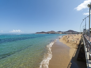 A beach with clear water, a sandy shore, and a promenade with railings. - Beachfront Apartment in Las Palmas by Las Canteras (Las Palmas de Gran Canaria)