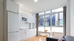 A modern kitchen with white cabinets, a microwave, and a dining area with a table and chairs. - Beachfront Apartment in Las Palmas by Las Canteras (Las Palmas de Gran Canaria)