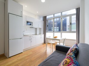 A modern kitchen with white cabinets, a microwave, and a dining area with a table and chairs. - Beachfront Apartment in Las Palmas by Las Canteras (Las Palmas de Gran Canaria)