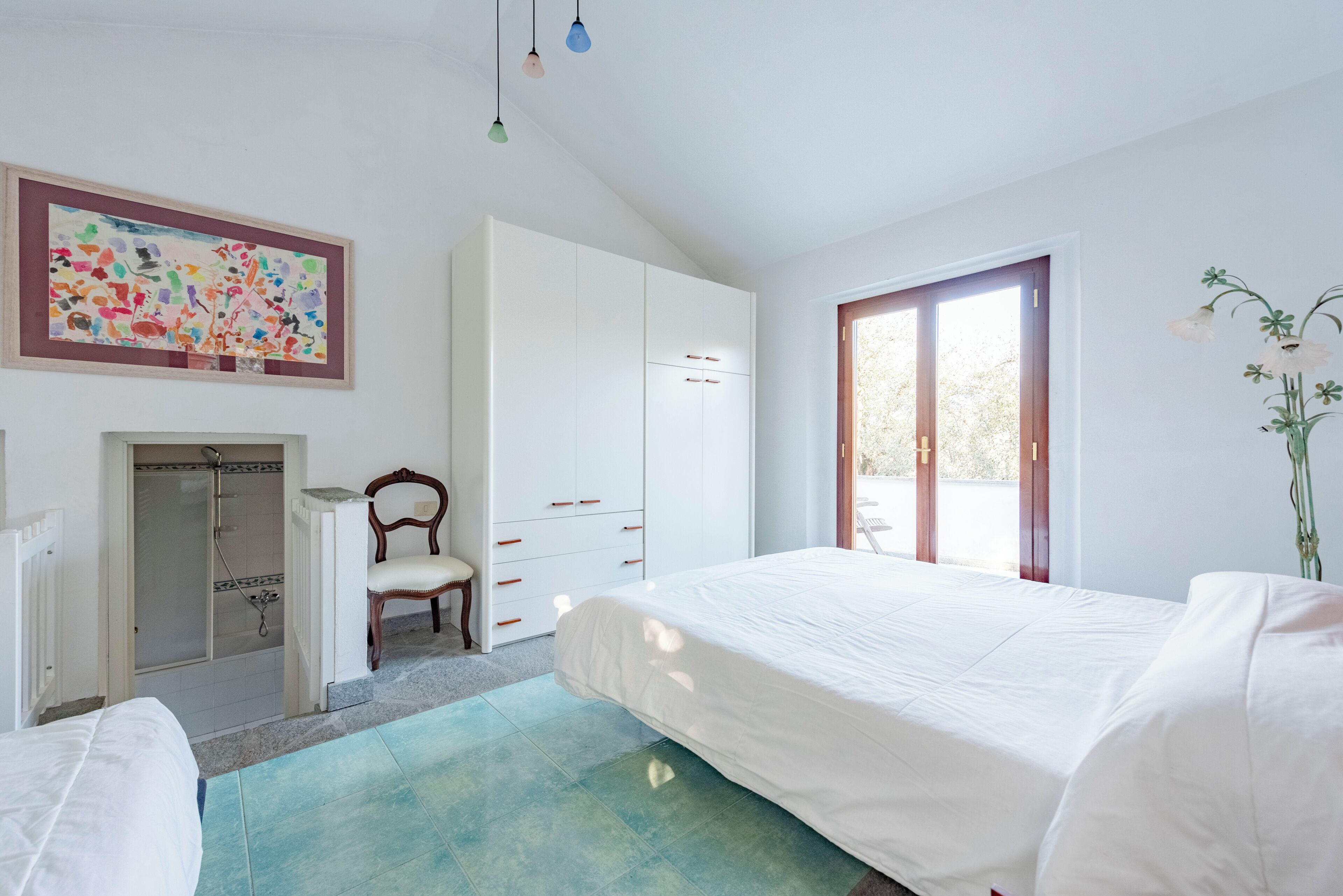 Ein Schlafzimmer mit Bett, Sessel, Kleiderschrank, Dusche und Fenster.