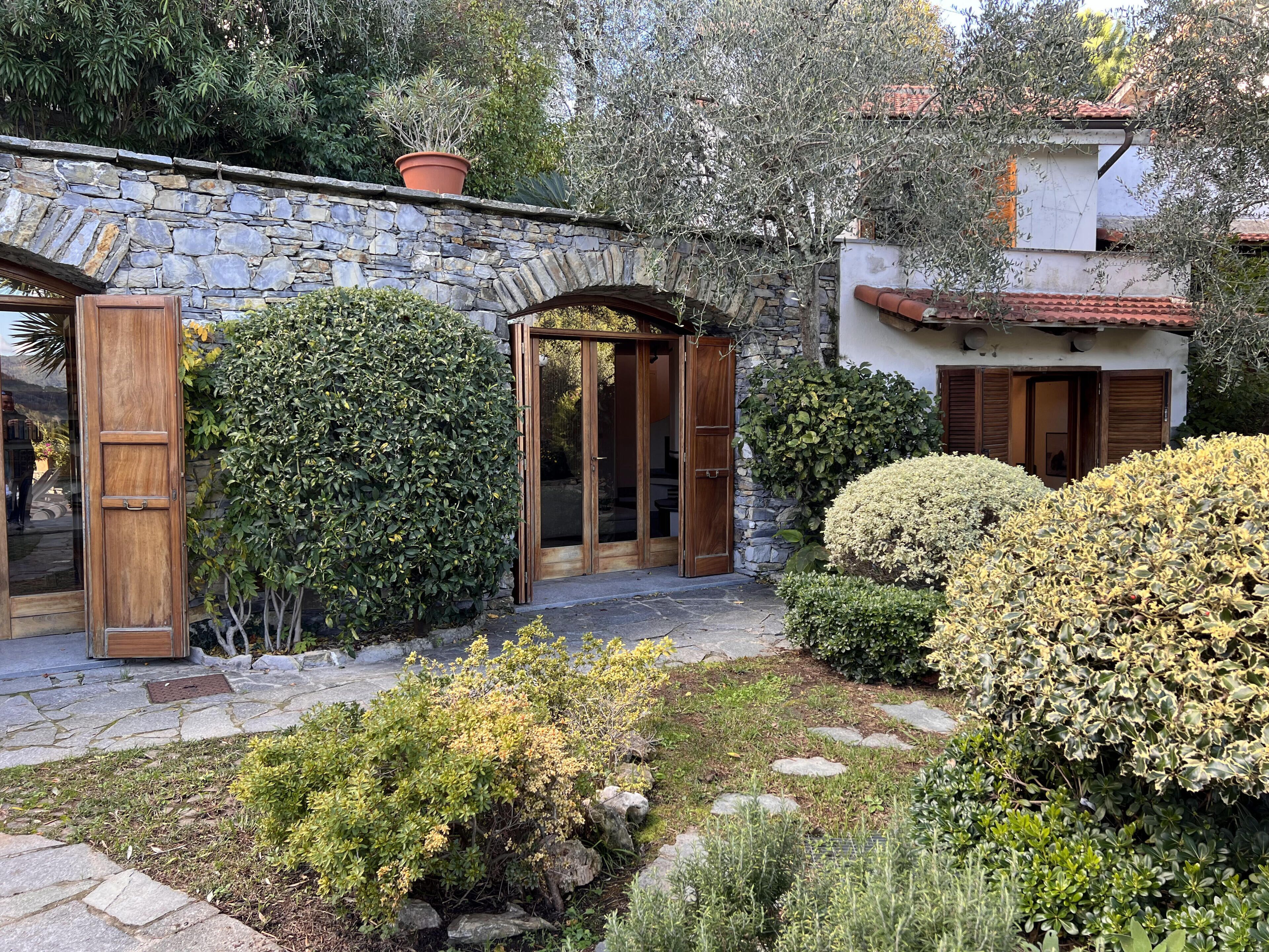 A stone building with a wooden door and a stone archway, surrounded by lush greenery and a stone pathway.