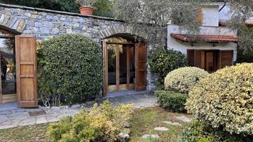 A stone building with a wooden door and a stone archway, surrounded by lush greenery and a stone pathway.