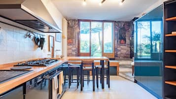 Una cocina moderna con estufa a gas, taburetes de bar, un muro decorativo de piedra y ventanas amplias.