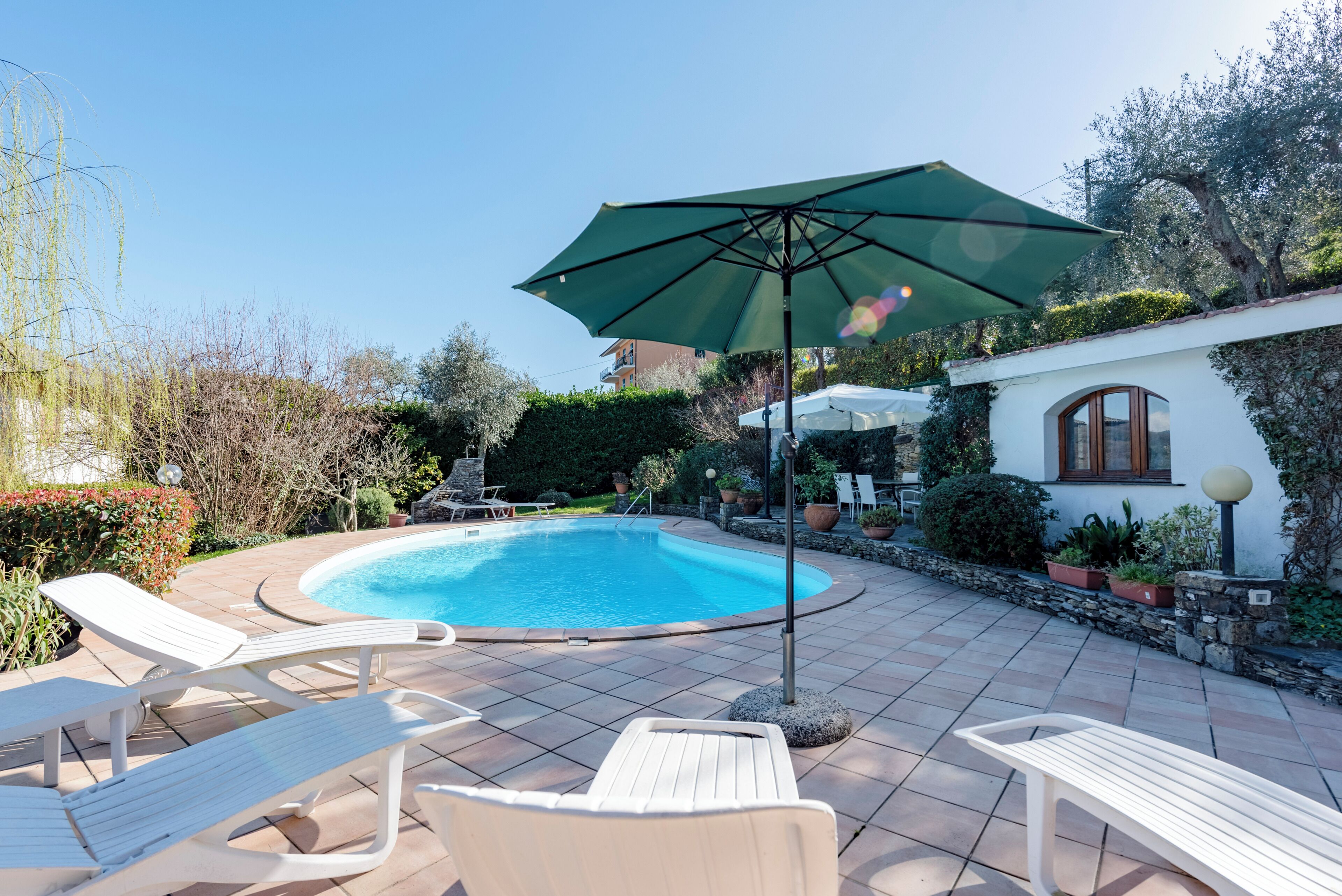 Une piscine entourée de verdure et d’un mur de pierre, avec des chaises longues et un parasol.