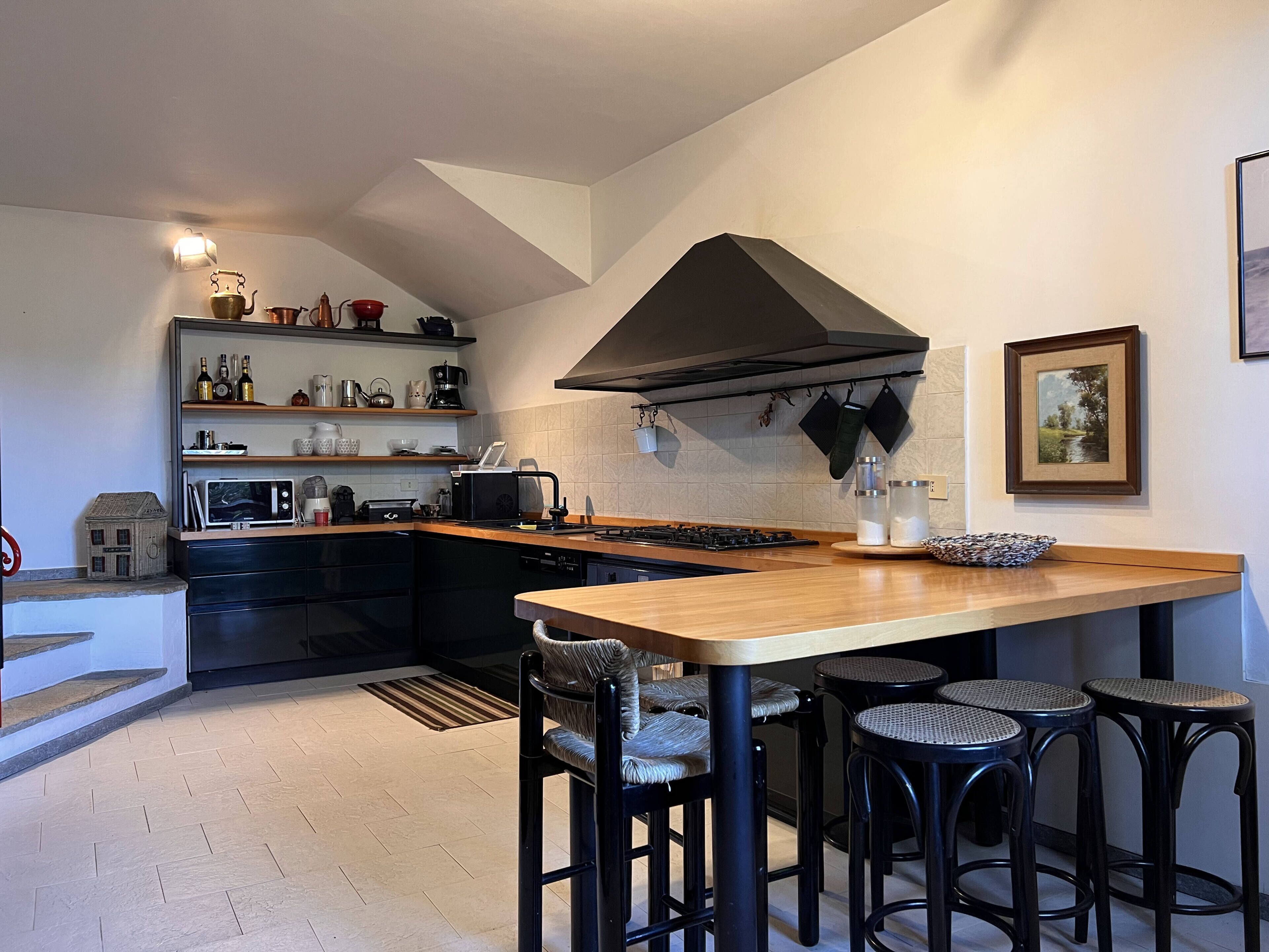 A modern kitchen with a central island, black bar stools, and a dining area.