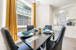 A modern dining area with a glass table, black chairs, and a view of the kitchen. - Super Deluxe 3 Bedroom Apartment (London)
