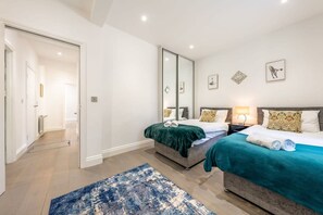 A hotel room with two beds, a large mirror, and a blue rug. - Super Deluxe 3 Bedroom Apartment (London)