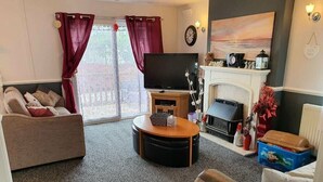 A living room with a sofa, a coffee table, a fireplace, and a television. - Cala Gran Holiday Park - Holiday Accommodation 9426 (Fleetwood)