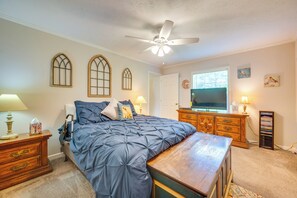 Une chambre à coucher avec un lit, une commode en bois, un téléviseur et un ventilateur de plafond.