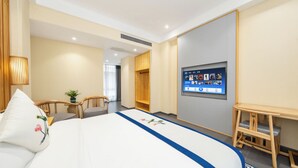 Habitación de hotel con una cama, un televisor montado en la pared, una silla de madera, una mesita y una planta en maceta.