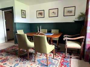 Un coin repas avec une table en bois, quatre chaises, un tapis à motifs et des œuvres d’art encadrées accrochées au mur.
