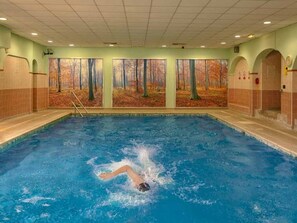 A swimming pool with a person swimming, surrounded by walls with large forest-themed murals.